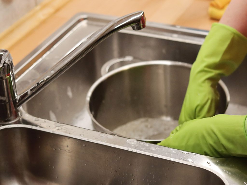 person cleaning dishes with fresh, soapy water and dish gloves