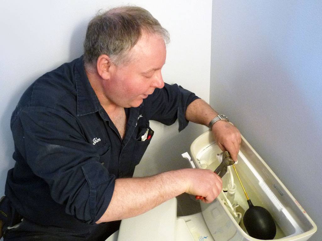 plumber working on back of toilet