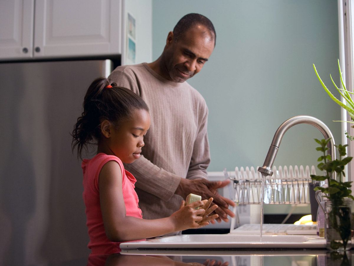 father and young daughter work to wash hands under kitchen sink facet