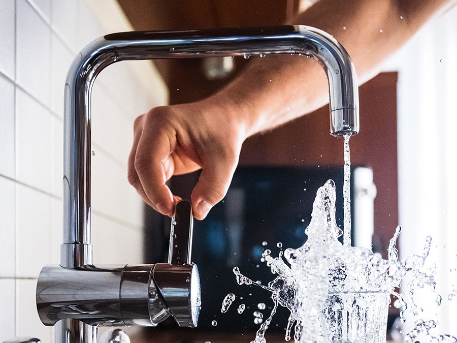 running faucet filling glass with fresh, drinkable water in kitchen