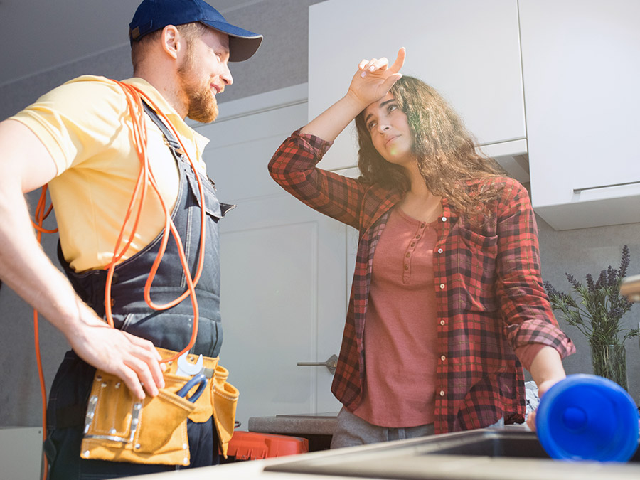 plumber and stressed out homeowner speaking together next to broken kitchen sink